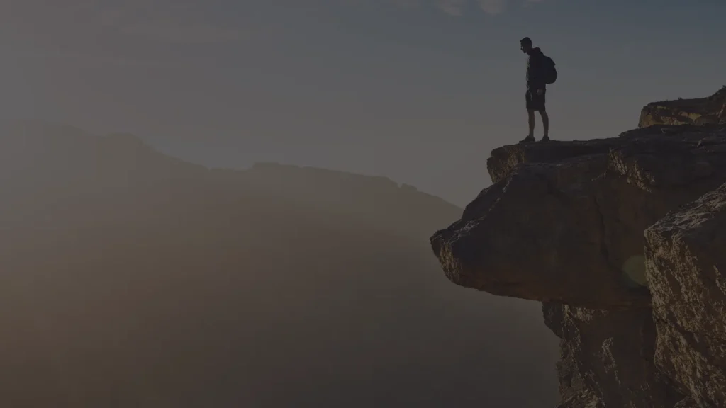 Man standing at the edge of a cliff representing the inner stillness presence offers before a high-pressure moment.