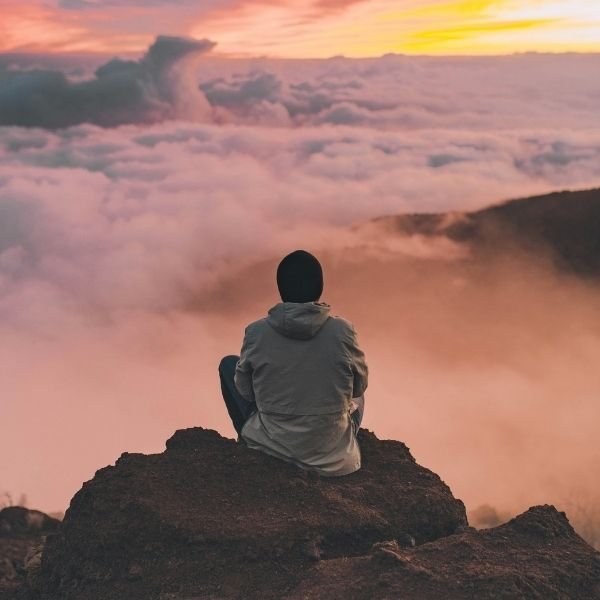 Person sitting still on a rocky ledge above the clouds at sunset, the traditional picture of meditation.